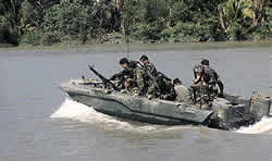 Soldiers are in a boat near a jungle area that could have been sprayed with Agent Orange