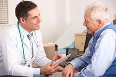 Photo of a younger male doctor talking with an older male patient.