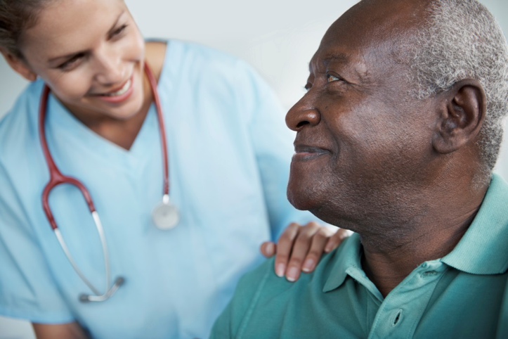 Female medical provider offers a hand of support to an older male patient.