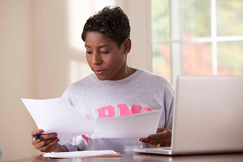 Woman with paperwork, at her laptop.